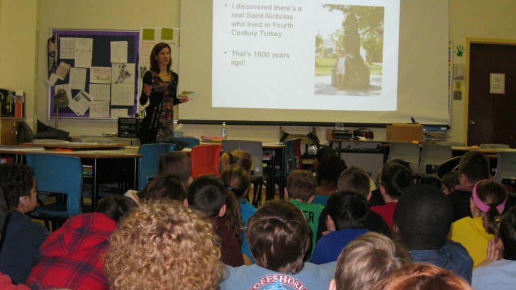 Karen speaks to a classroom of children sitting on the floor, with an image projected on the whiteboard.