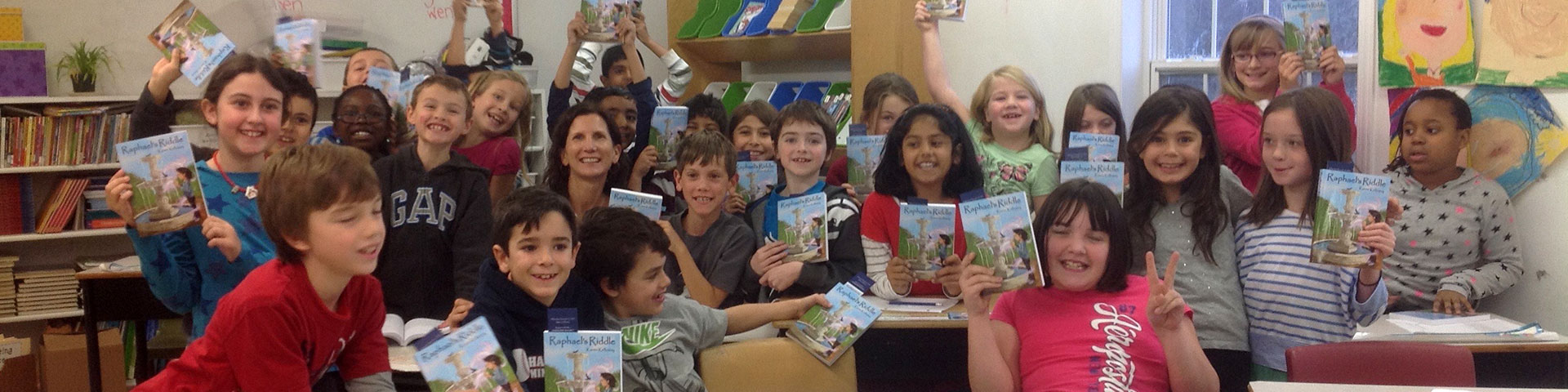 Karen smiles amongst school children who hold up copies of Raphael's Riddle